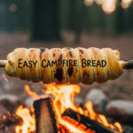 A close-up of a perfectly golden, fluffy easy campfire bread on a stick, held over a warm, glowing campfire.